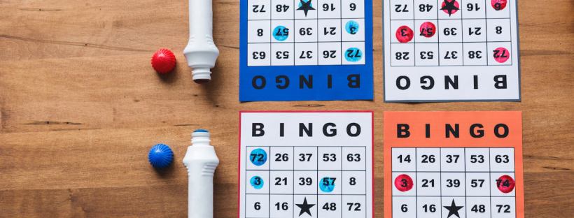 A blue bingo daubber and a red bing daubber are place on a table mirroring each other with two bingo cards on either side of them.