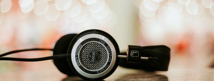 A pair of headphones sit on a table with bright lights out of focus in the background