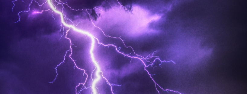 Strong bolts of lightning light up a dark, purple cloudy sky